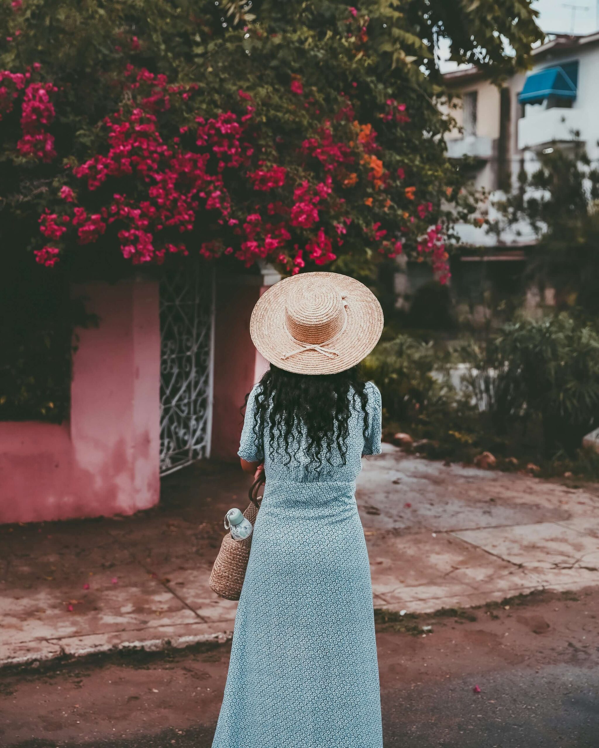 Woman in a blue dress and hat walking near a flowering tree, symbolizing MitoKhon's human-centered and equitable philosophy of care.