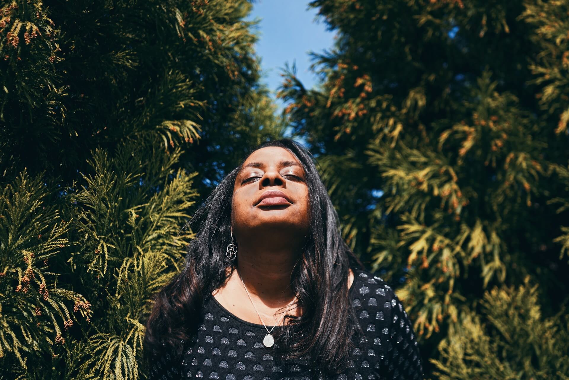 Confident woman standing outdoors, basking in sunlight amidst trees, symbolizing MitoKhon's Professional Transformation services for leadership development.