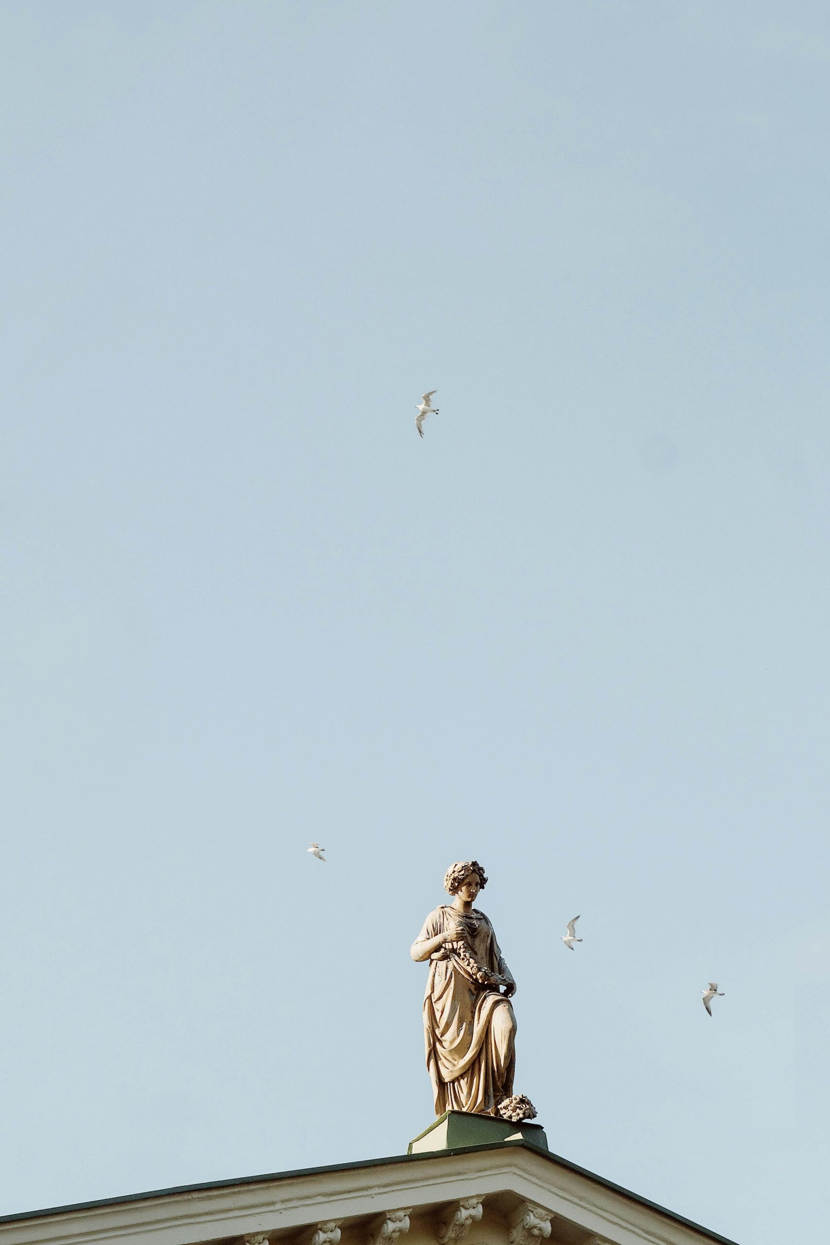 Statue on a building with a clear blue sky and birds in flight, symbolizing MitoKhon's Strategic Advisory services focused on leadership and operational excellence.